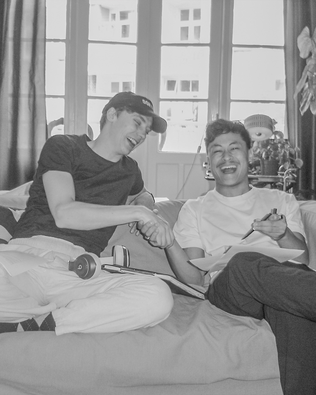 two friends laughing together on a sofa with a notebook